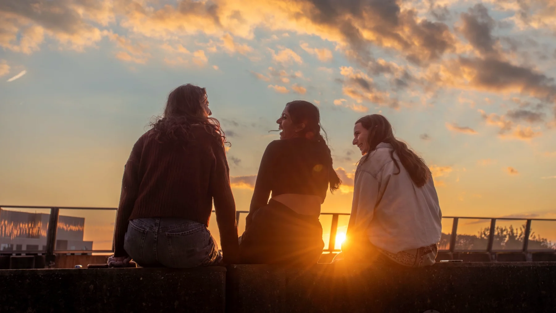 Three female students sitting on wall watching the sunset.